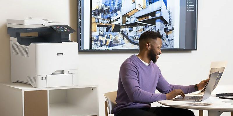 Hommes travaillant sur un ordinateur portable devant une Imprimante couleur multifonctions Xerox&reg; VersaLink&reg; C415