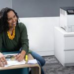 Femme souriante dans un bureau à côté de l'imprimante couleur Xerox® VersaLink® C620