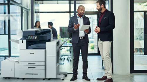 Deux hommes dans un bureau discutent sur une tablette à côté d'une imprimante multifonction couleur Xerox® AltaLink® série C8200