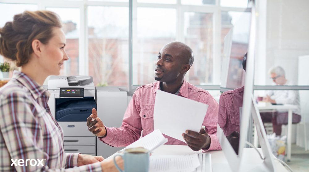Une personne examine des données sur l'écran d'un ordinateur portable, avec une superposition numérique de diverses icônes d'appareils (imprimantes, appareils mobiles) et de lignes connectées, symbolisant la gestion centralisée de la flotte pour Xerox Workplace Solutions.